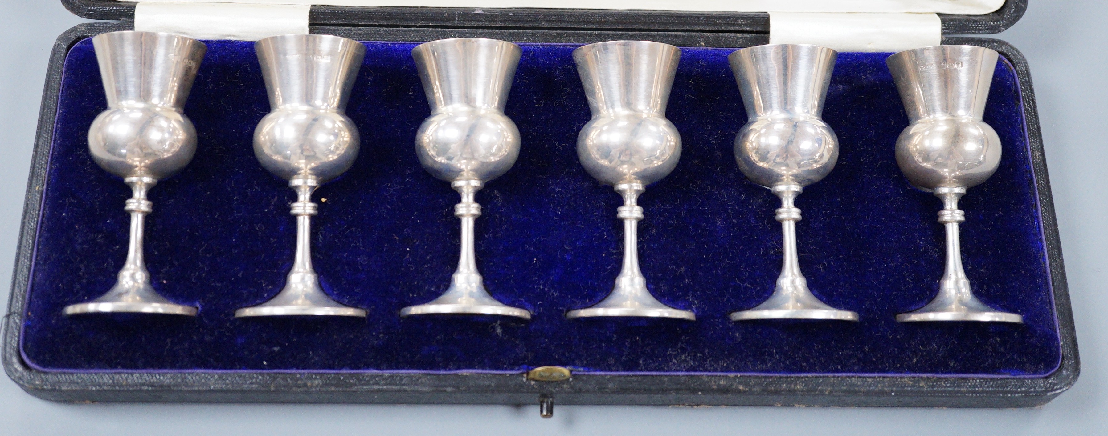A cased set of six George V silver thistle shaped pedestal tots, E.S. Barnsley & Co, Birmingham,1911, 83mm.